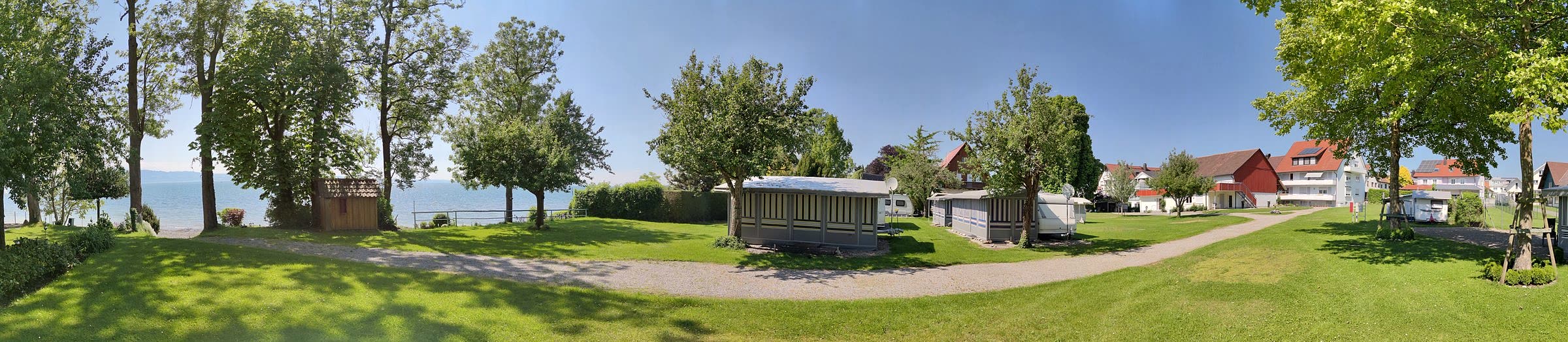 Panorama des Campingplatzes Nonnenhorn: Bäume und Seeufer links, Stellplätze in der Mitte, Gebäude rechts