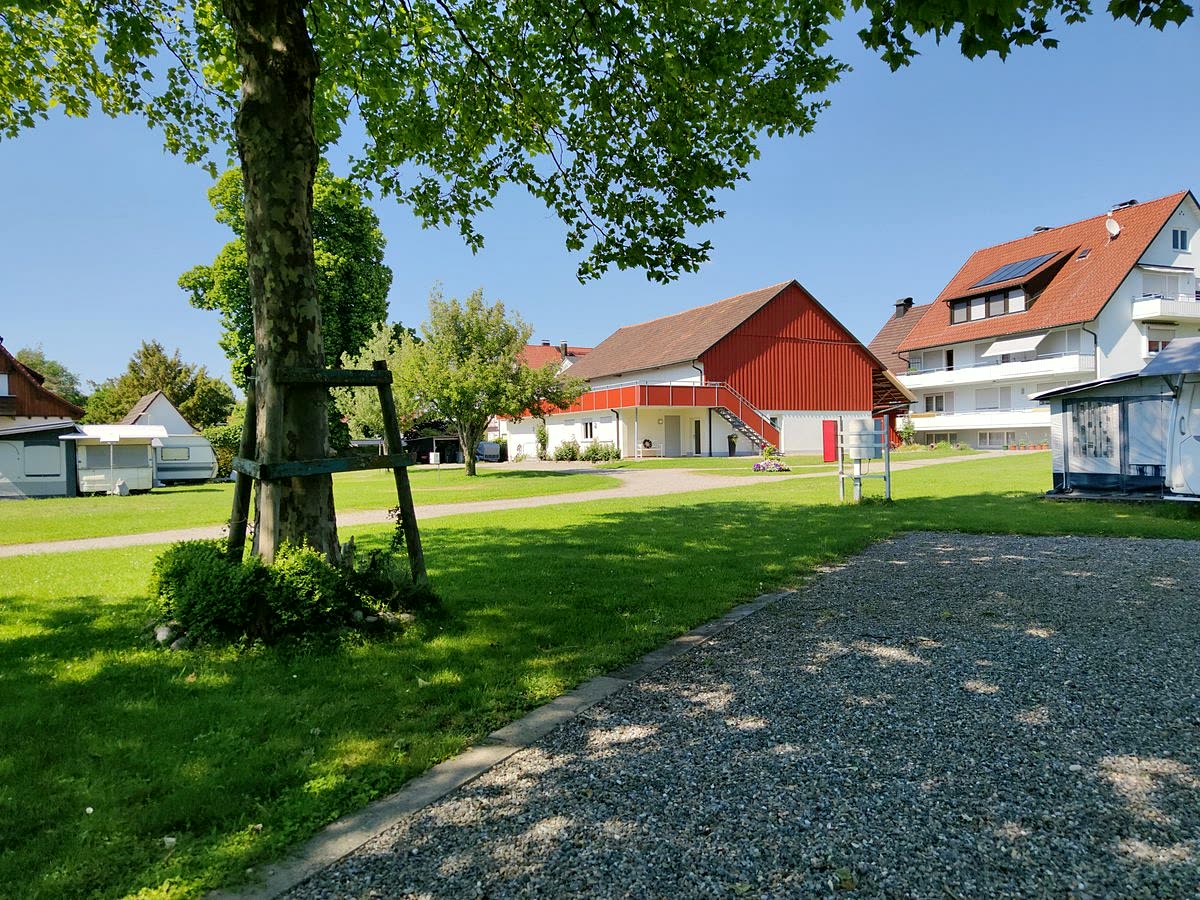 Blick über die Wiese auf die rote Scheune und das Wohnhaus des Campingplatzes